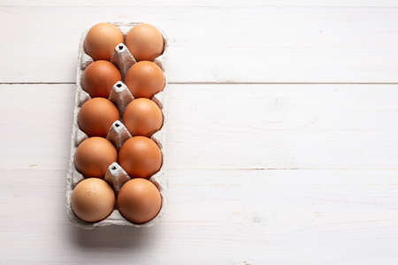 Fresh organic chicken eggs in carton pack or egg container on white wood background. Space for text.