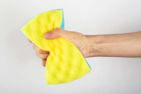 A female hand holds a cleaning sponge on a white background. Cleanliness concept. Indoor cleaning.の写真素材
