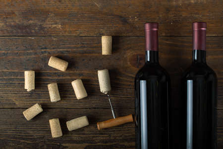 Glass wine bottle with corks and corkscrew on wooden table background. Top view.