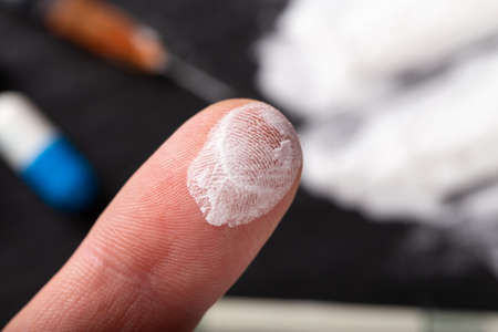 Human finger in cocaine or other drug. In the background are tablets, a syringe, money, drugs. Selective focus.の写真素材