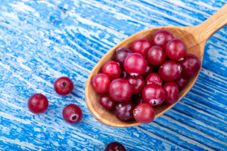 raw cranberries on a wooden table in a simple wooden spoon