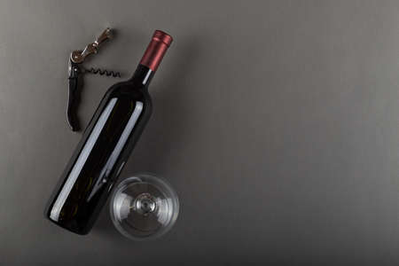 Corked red wine bottle, corkscrew and empty wine glass on gray background. Alcoholic drink. Winemaking concept. Space for text. Top view.の写真素材