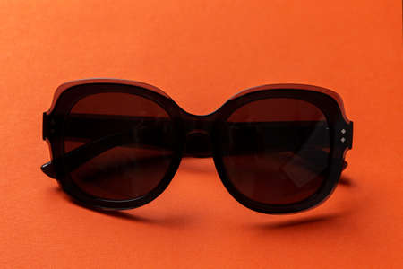 Black sunglasses on orange background, top view, flat lay, minimalistic concept of summer, vacation.