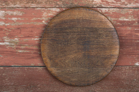 Circle cutting board on a red wooden table. Food preparation tool and kitchen utensils. Space for text.の写真素材