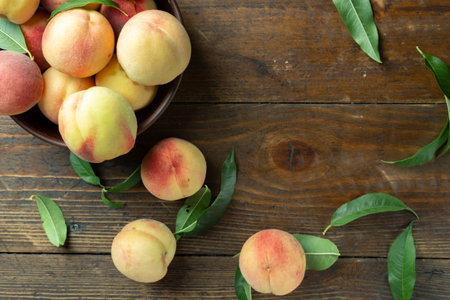 Fresh sweet peaches on the wooden table, selective focus. Fresh ripe peaches with leaves in a bowl on a wooden background.の写真素材