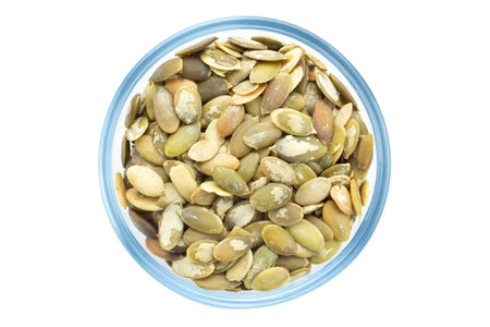 Peeled pumpkin seeds in a bowl, top view. Isolated on white background. File contains clipping pathの写真素材