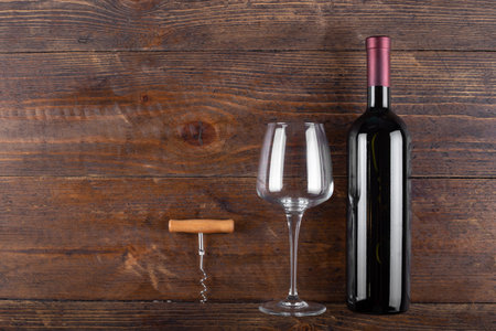 Bottle of red wine, a corkscrew and an empty glass on a wooden background. Space for text. Top view.の写真素材