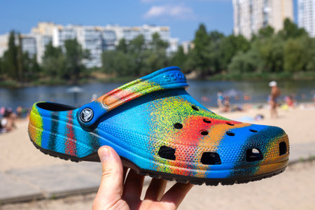 Ukraine, Kyiv - July 04. 2022: multi-colored Crocs in hand close-up. In the background, the sand...
