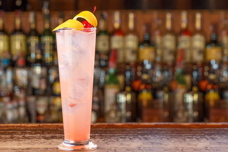 Glamorous alcoholic cocktail on the bar. A pink drink with lots of ice, and a beautiful garnish of lemon peel and cherryの写真素材