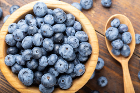 Ripe blueberries in a wooden bowl and spoon on a background of scattered berries. Concept of healthy and dieting eating. Side viewの写真素材