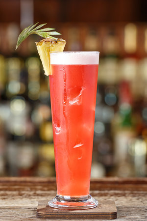 Singapore sling cocktail with gin, cherry and orange liqueur Benedict, grenadine, pineapple and lemon juice with the addition of bitter Angostura. Cocktail on the background of the bar in the nightclubの写真素材