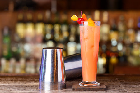 A barman shaker and a cocktail stand on a wooden bar counter in a nightclubの写真素材