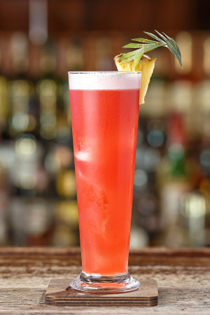 Singapore sling cocktail with gin, cherry and orange liqueur Benedict, grenadine, pineapple and lemon juice with the addition of bitter Angostura. Drink on the background of the bar in the nightclubの写真素材