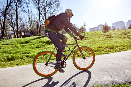 A cyclist rides on the road to the city on a background of green grass and buildings. Spring in the city. Eco-friendly mode of transportの写真素材