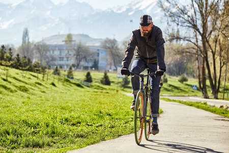 A cyclist rides on a road in the city against a background of green grass and mountainsの写真素材