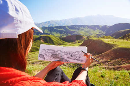 The girl holds in her hands a picture of a mountain landscape. Kazakhstan. Mountain spring landscape
