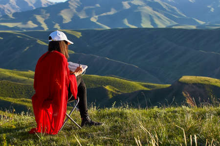 Girl draws on nature spring landscape. Painting outdoors. Kazakhstan. Mountain landscapeの写真素材
