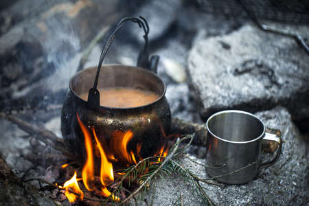 Tea with milk cooked at the stake. A kettle, a metal mug, a fire. Traveler's breakfastの写真素材