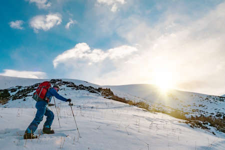A man is engaged in skituring on split snowboarding. Sunrise is sunny in the mountains