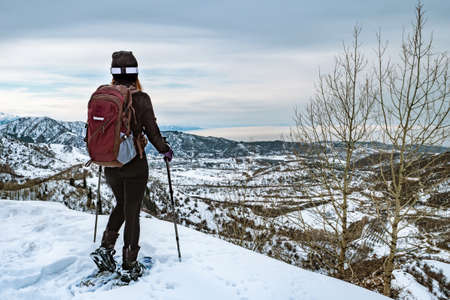 Hiker in the mountains walk on snowshoes. The girl on the edge of the hill look into the distance. View from the back. Winter mountain tourism. Kazakhstanの写真素材