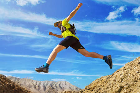 The athlete runs off-road. Jumps over a ravine. Trail runner in the desert. A man wearing a yellow T-shirt and shorts. National Park Altyn-Emel. Kazakhstanの写真素材