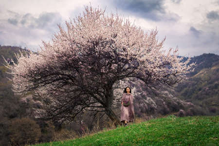 Asian girl walking in the spring outdoors. A girl walks across a green field under the crown of a...