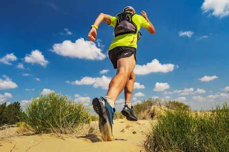 Athlete runs along the sandy desert. Desert trail running. A man in shorts and a T-shirt is running...