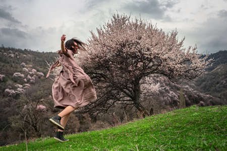 Girl joyfully whirls outdoors among flowering trees. Spring time. A girl with long hair. On the girl a long linen dressの写真素材