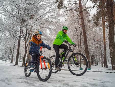 A father and his son ride a bikes in a winter park. Weekend in a snowy parkの写真素材
