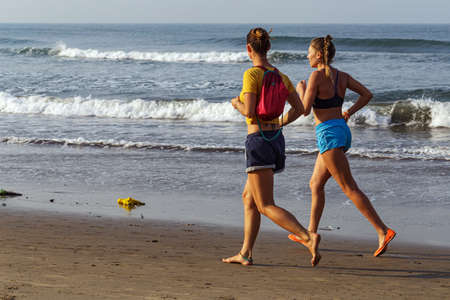 ARAMBOL, GOA, INDIA - JANUARY 20: Young women jogging in the early morning by the sea. Arambol, Goa,...