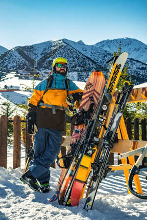 Ski resort Chunkurchak, Tatyr village, Kyrgyzstan - DECEMBER 23, 2018: A bearded guy in a helmet and glasses stands near a rack with skis and snowboards. Beautiful sunny dayのeditorial素材