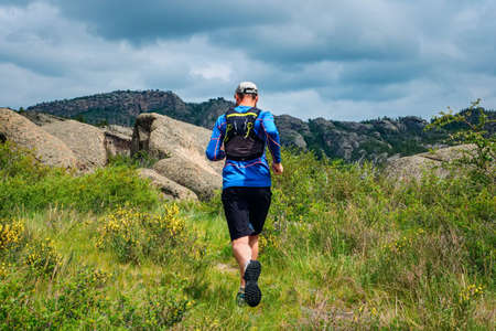 Athlete runner running on a mountain trail. Male runs in the mountains among the rocks. View from...