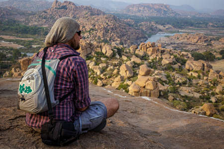 Tourist guy sitting on the edge of a hill. Beautiful view of the amazing Hampi's ruins. Beautiful view of the amazing Hampi's ruins. Karnataka, Indiaの写真素材