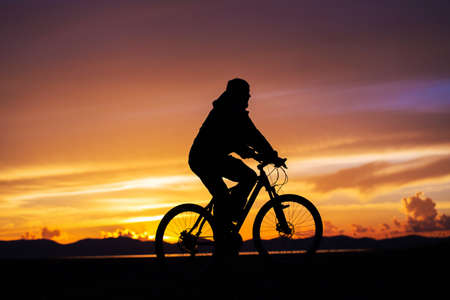 Silhouette of a cyclist rolling on the background of a beautiful sunset. A magnificent evening in the mountainsの写真素材
