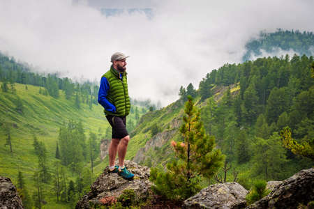 A man stands on a hill in front of a foggy mountain valley. Foggy weather high in the mountains in...
