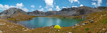 Panorama with a yellow tent on the shore of a mountain lake framed by rocky mountains. Kazakhstan, Kensu gorgeの写真素材