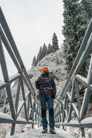 Bearded male traveler walks outdoors in winter. A guy stands on a bridge over a mountain river....