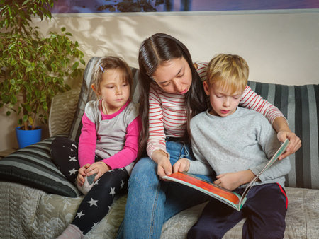 Girl nanny reads a book to children. Working with children at home. Education and pastime with childrenの写真素材