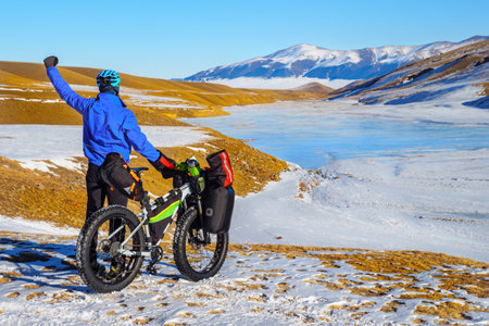 Male traveler on a bicycle in winter in the mountains. Winter travel. High-mountain plateau Turgen-Asy, Kazakhstanの写真素材