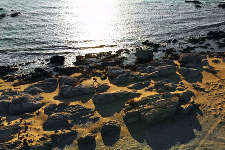 The guy runs along the beach. He jumps from stone to stone. Running offroads. Trail running. aerial photographyの写真素材