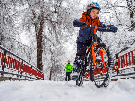 A boy rides a bicycle in a winter park under the supervision of his father. Wonderful winter day outdoors after snowfallの写真素材