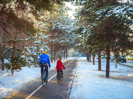 Father and son ride bicycles on the bike path in winter. Cycling as a sustainable and healthy form of urban transportの写真素材