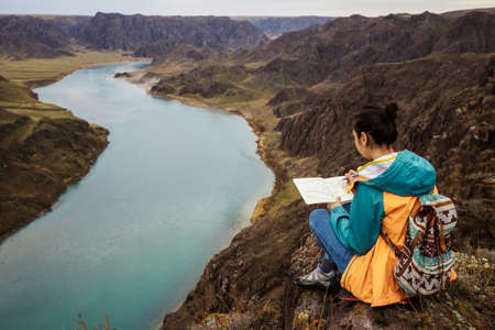 Girl draws on nature spring landscape. painting outdoors. Plein air painting. A girl sits on a rock by the river. Ili River. Kazakhstan.の写真素材