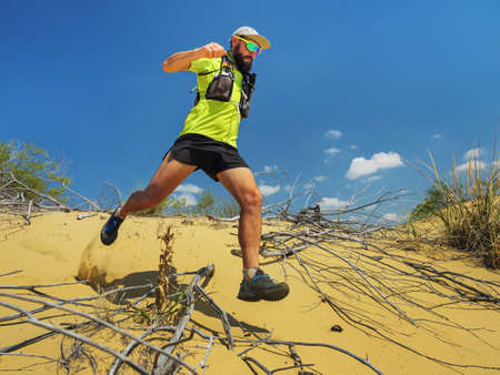 Athlete runs along the sandy desert. Desert trail running. A man in shorts and a T-shirt is running...