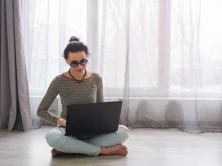 A woman sitting on the floor in the apartment, opened a laptop in front of her. home office conceptの写真素材