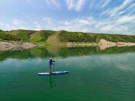 A bearded man swims on a SUP board on a lake among the rocks. Stand Up Paddling. Mountain lake with azure waterの写真素材
