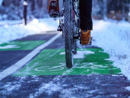 Bicycle wheels ride along a bike path on a winter evening. Bicycle road sign on the asphalt and a cyclist riding on the roadの写真素材