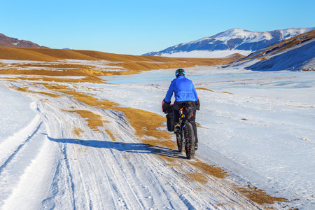 A male traveler rides a fat bike in the mountains in winter. Winter trip. High mountain plateau Turgen-Asy, Kazakhstan.の写真素材