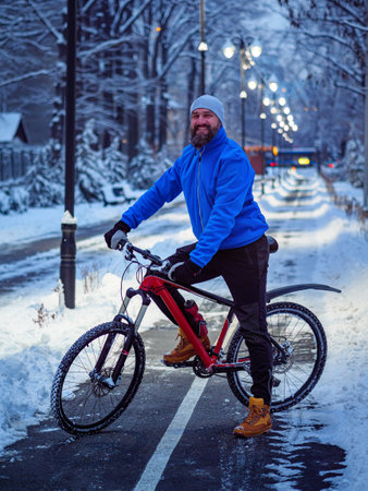 Bearded man with a bicycle in a winter city late in the evening. Active and healthy lifestyle in the city. Smiling man in a blue jacket with a red bicycleの写真素材