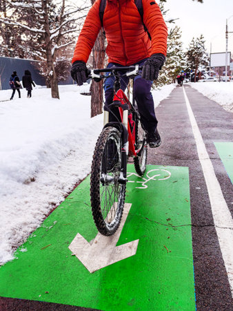 A man on a bicycle wearing an orange jacket rides on a bike path in winter. The cropping hides the man's face. Ecological transportation in the cityの写真素材
